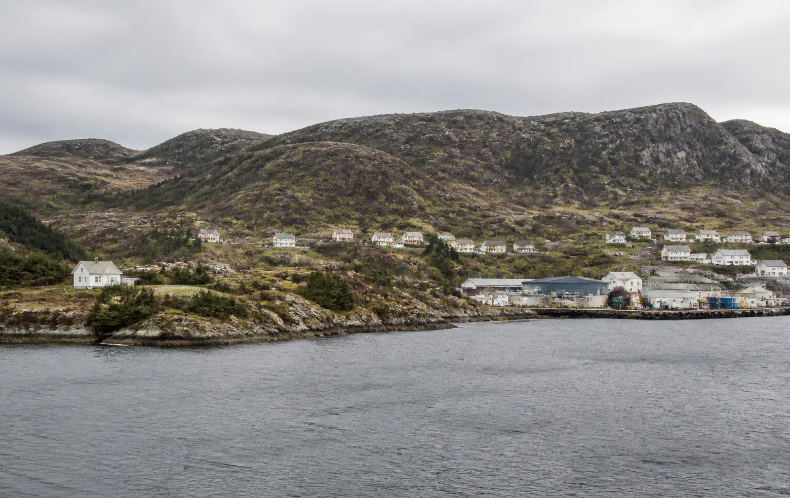 Kystlandskap i Sunnhordland med bustadfelt og industrikai under grå himmel